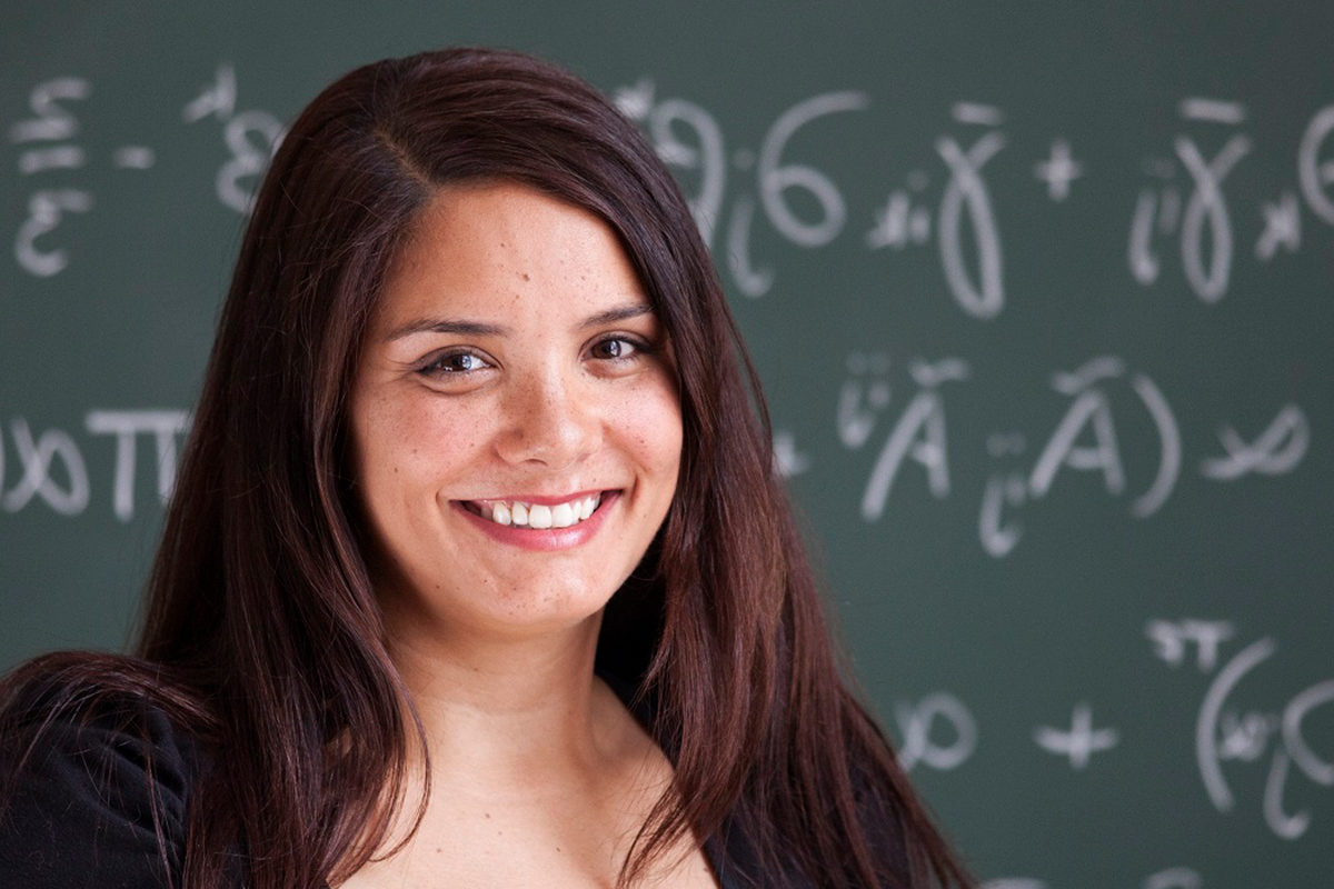 A postgraduate mathematics student smiles in front of a whiteboard with mathematical equations