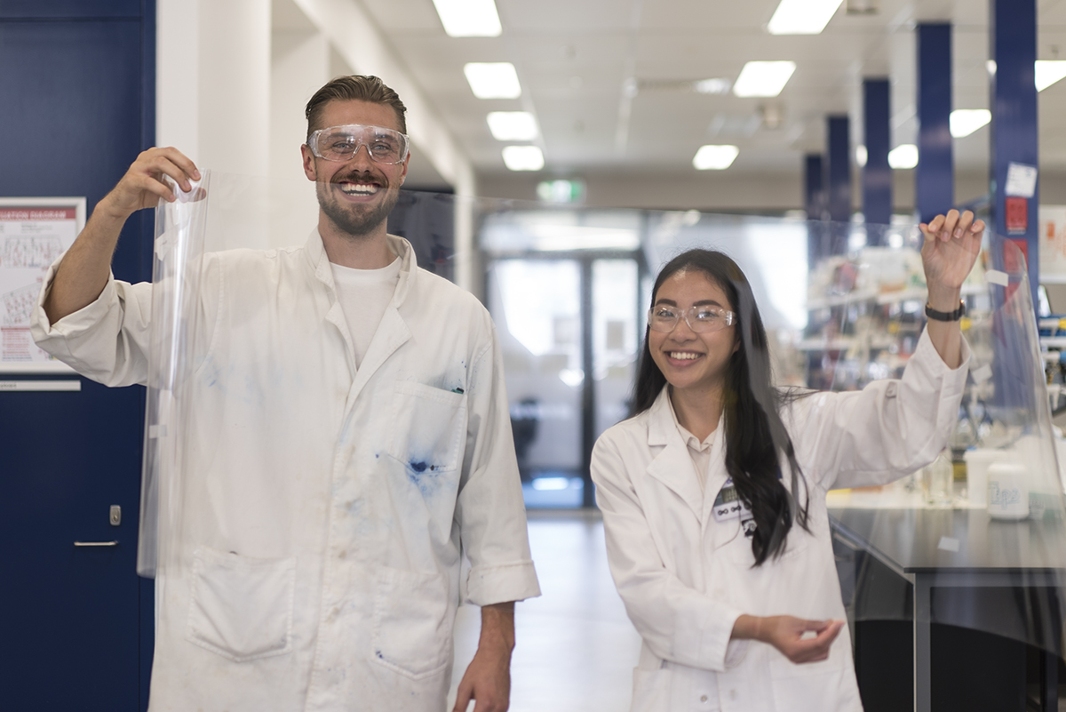 Matthew Spence and Vanessa Vongsouthi stand behind a sheet of PET plastic film, the breakdown target of their PETase enzyme. 
