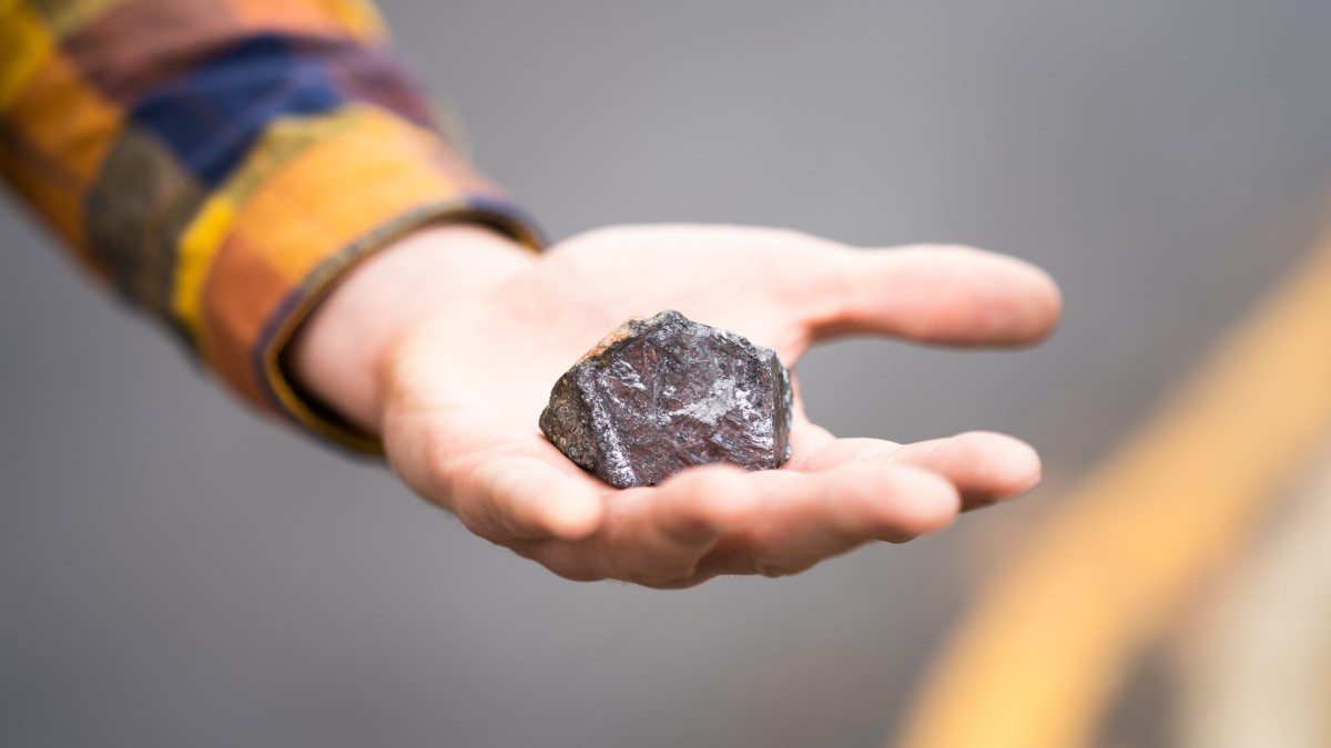 A hand holding a chunk of grey rock.