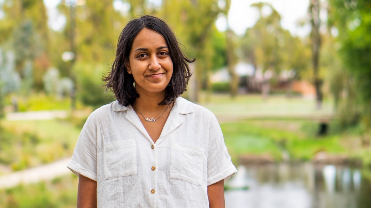 A woman in a white shirt standing in front of a creek and trees