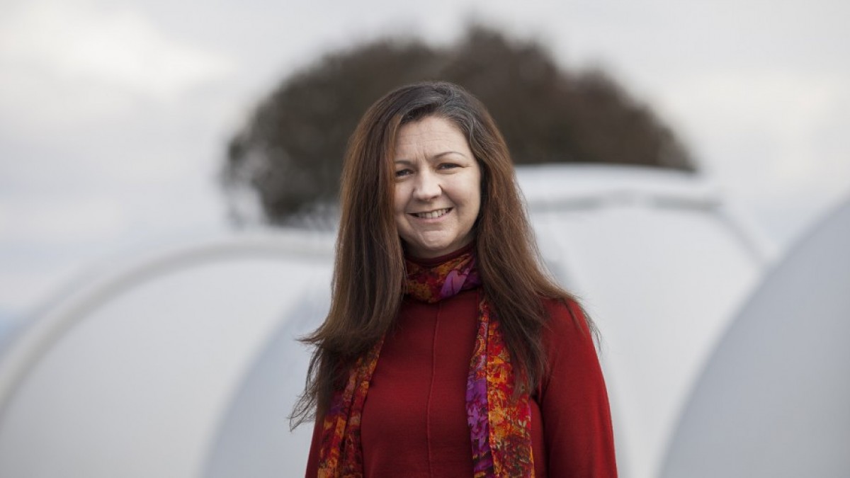 Professor Lisa Kewley standing in front of telescopes.