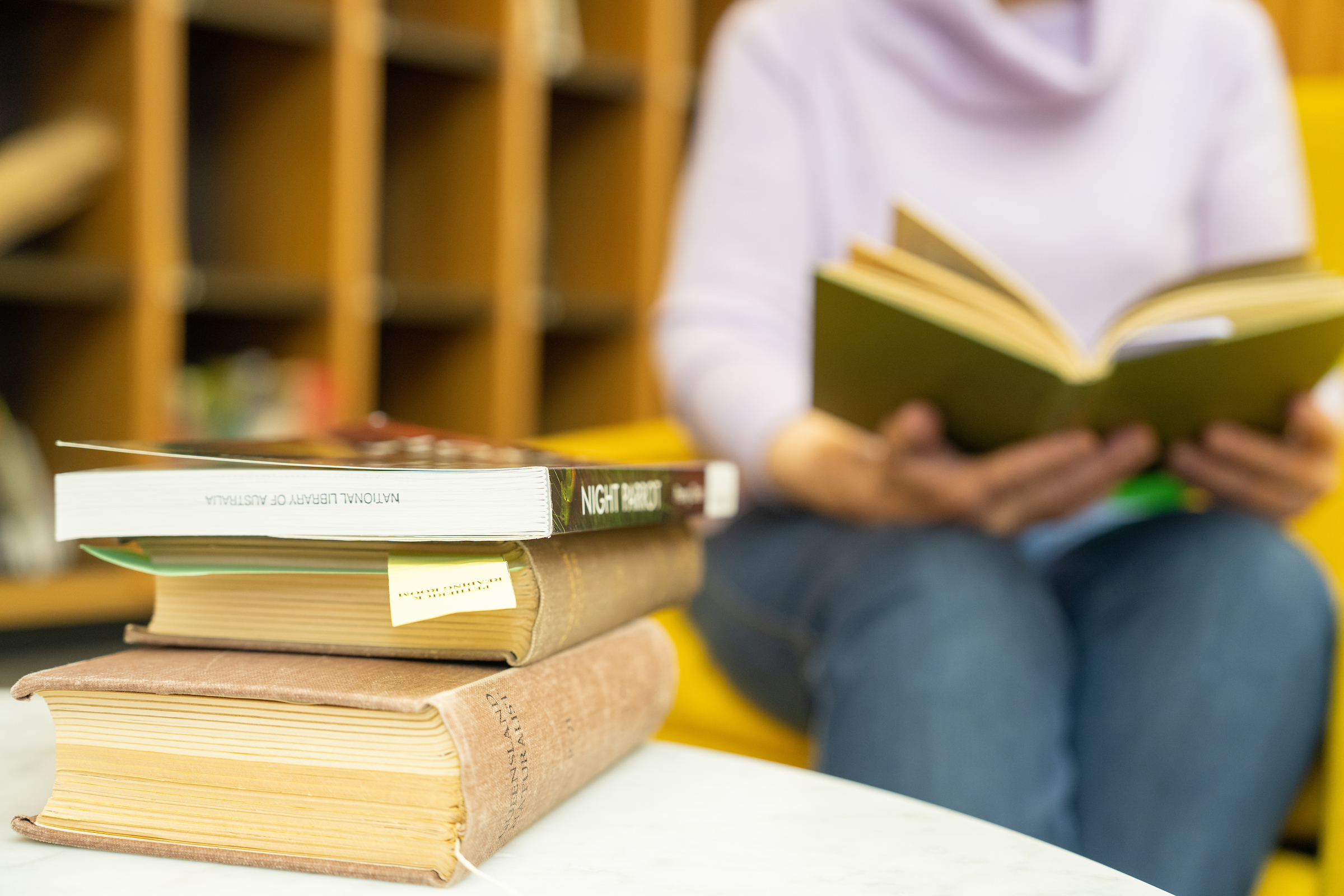 Three books stacked on a table and a faceless woman reading