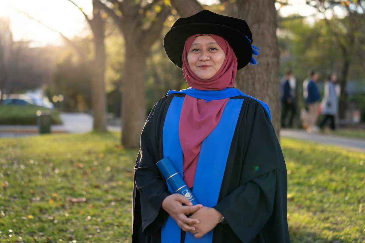 Dr Aini Jasmin Ghazalli. Photo: ANU/Nic Vevers A woman in graduation robe standing outdoors