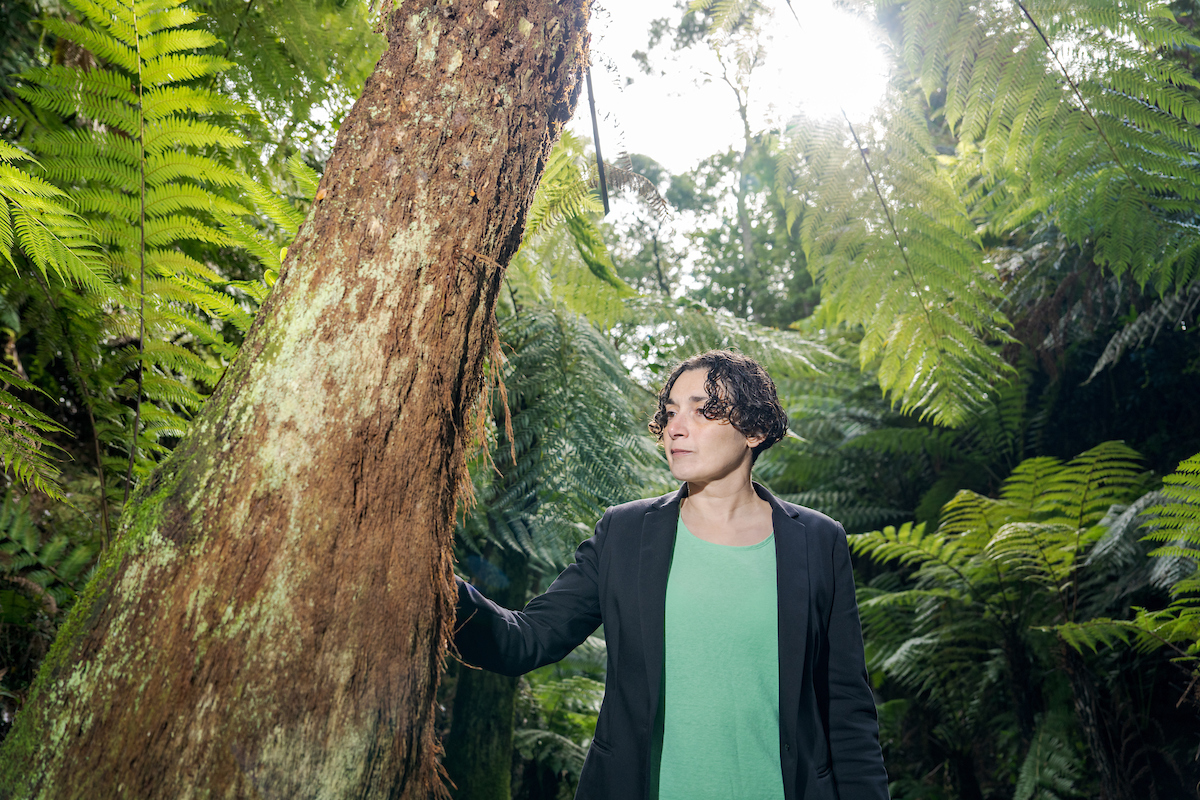 Photo: Nic Vevers/ANU Dr Joëlle Gergis is standing in a rainforest. Her right hand is on a large tree trunk.