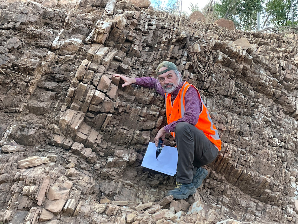 Professor Jochen Brocks inspecting the 1.6-billion-year-old rocks in Australia’s Northern Territory. The rocks contained a primordial chemical structure that hinted at the existence of the Protosterol Biota. Photo: Professor Jochen Brocks/ANU Man next to rock shelf in hi-viz