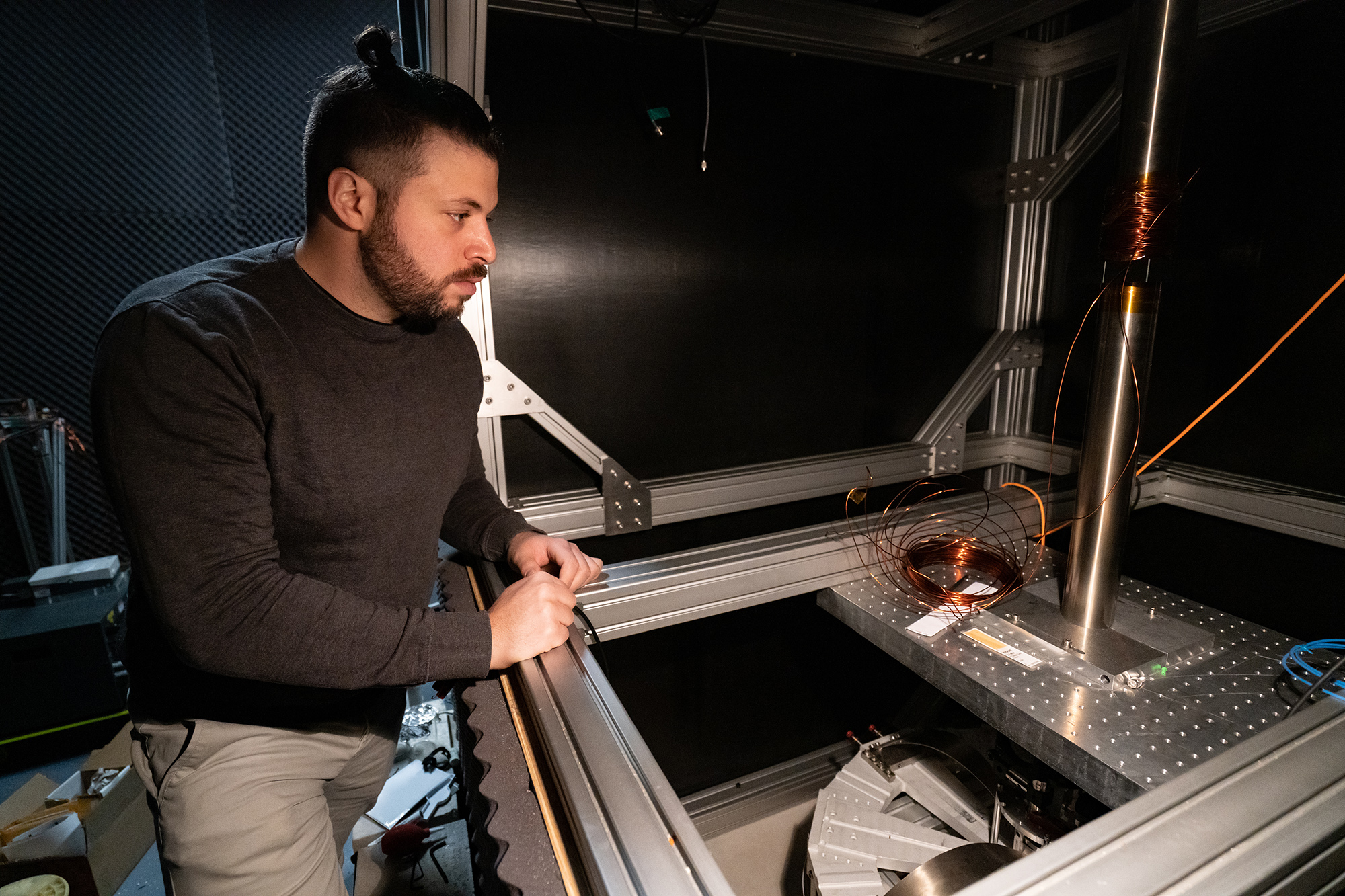 PhD student Yosri Ben Aicha inspects the atomic gravimeter at the ANU Research School of Physics. Photo: Nicholas Vevers/ANU. Man wearing a dark grey shirt looking into atomic gravimeter technology inside a physics laboratory.
