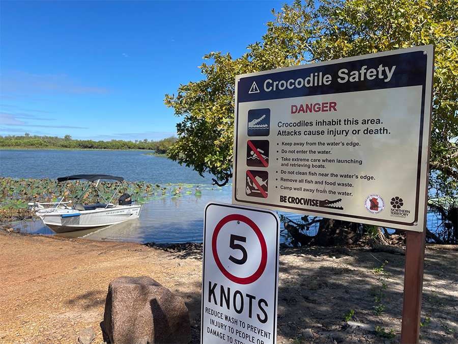 Sign describing Crocodile Safety by a riverbank and a dinghy