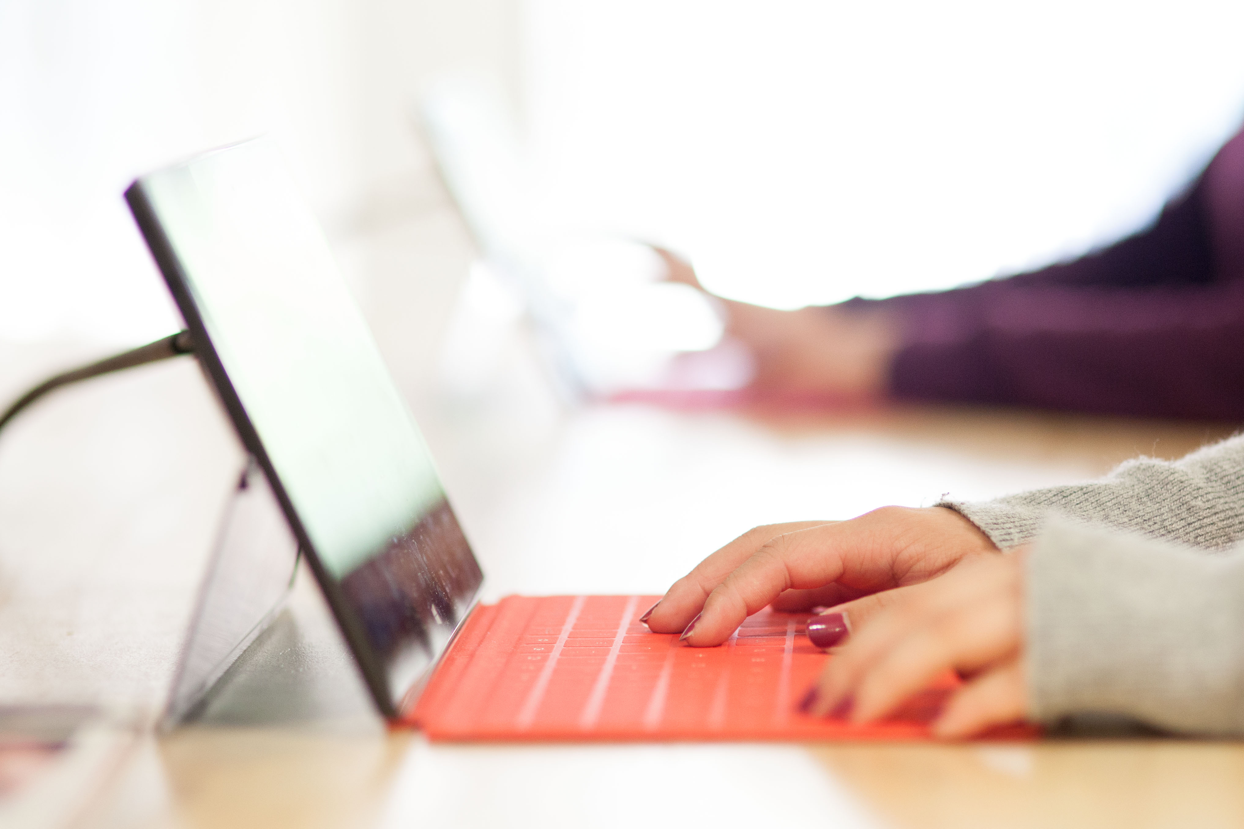 A person's hands typing on a bright red keyboard attached to a tablet on a table with soft background lighting.