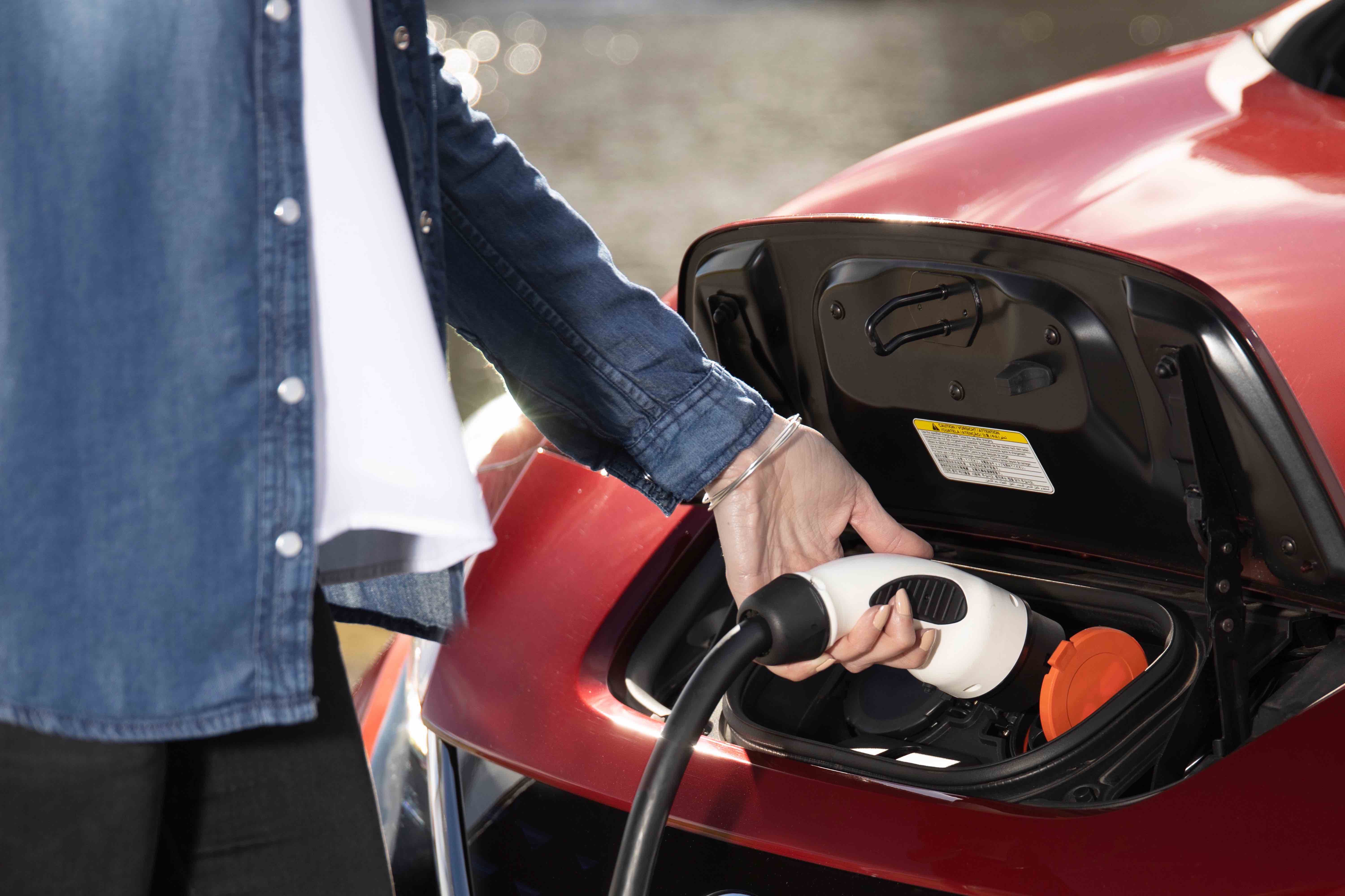 Person charging an electric car by plugging in a charge connector.