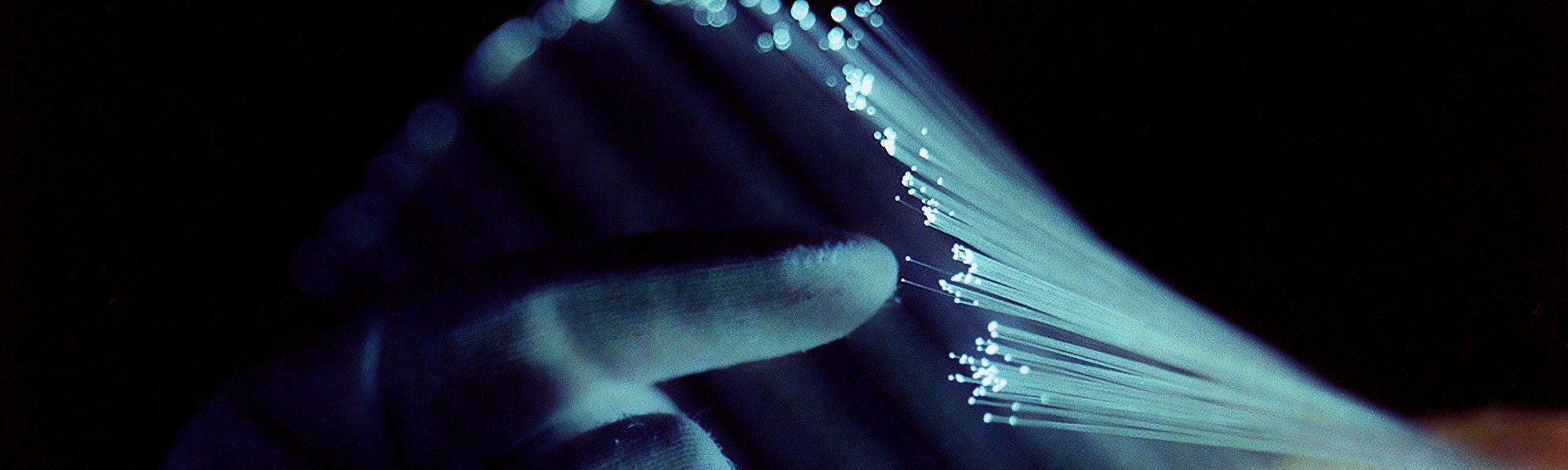 A close-up image showing a hand interacting with strands of illuminated fiber optic cables in a dark setting.