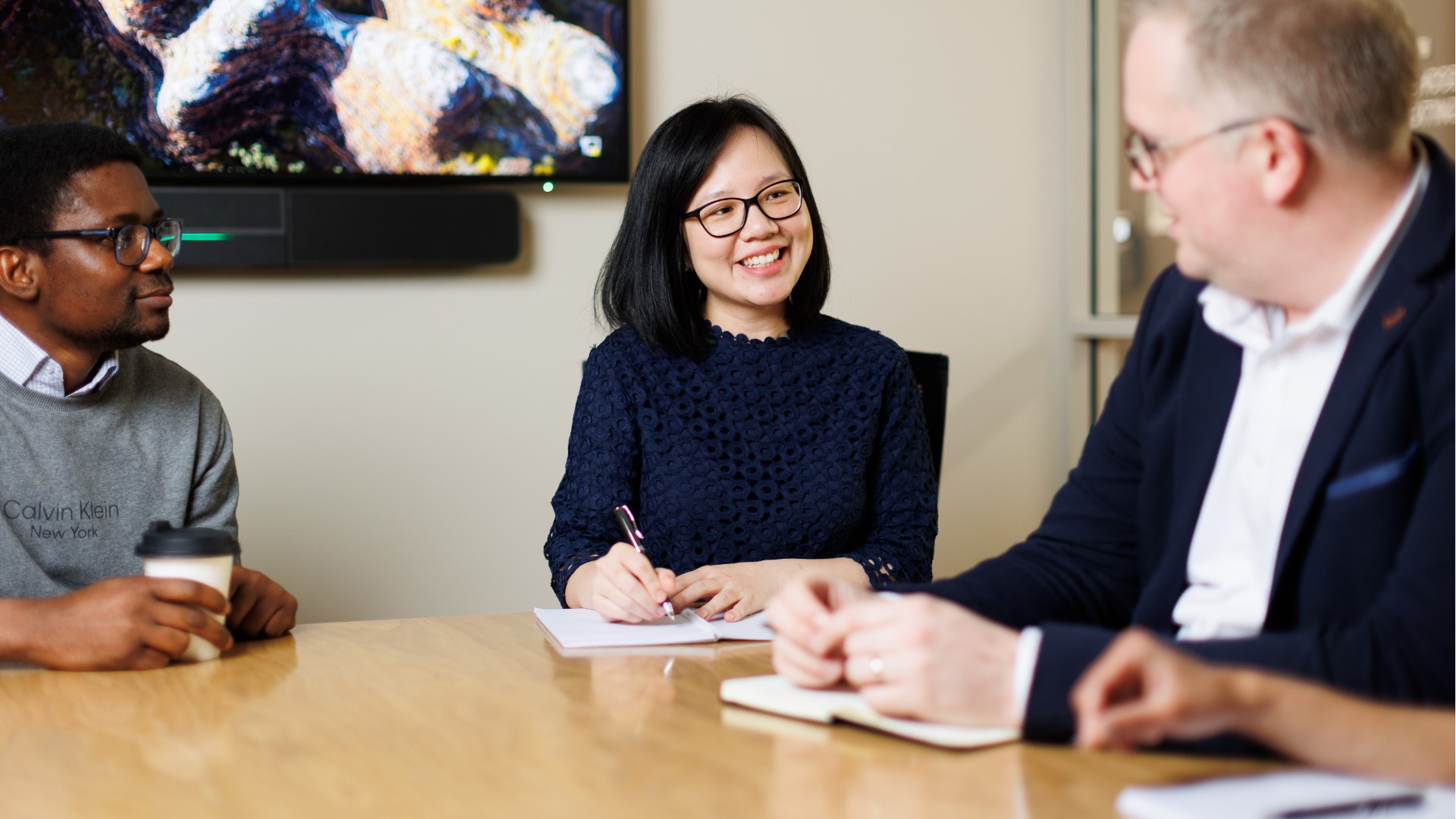 Three professionals engaged in a conversation around a table in a modern office setting.