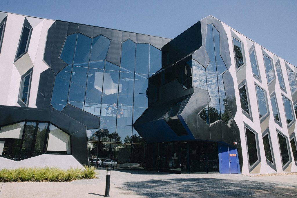 Modern building with a reflective glass facade and unique geometric white frames under a clear blue sky.