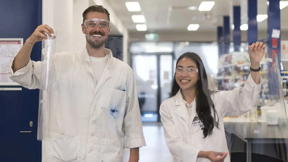 Matthew Spence and Vanessa Vongsouthi stand behind a sheet of PET plastic film, the breakdown target of their PETase enzyme.