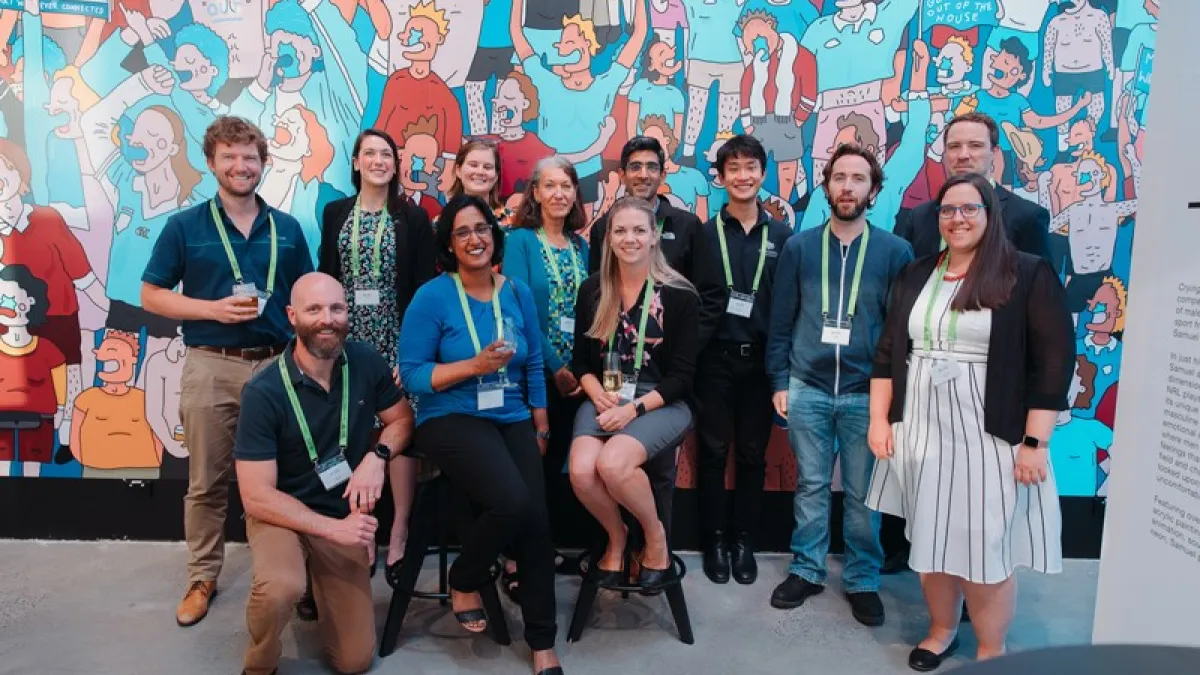 A group of professionals smiling for a photo at a conference with a colorful cartoon-style mural in the background.