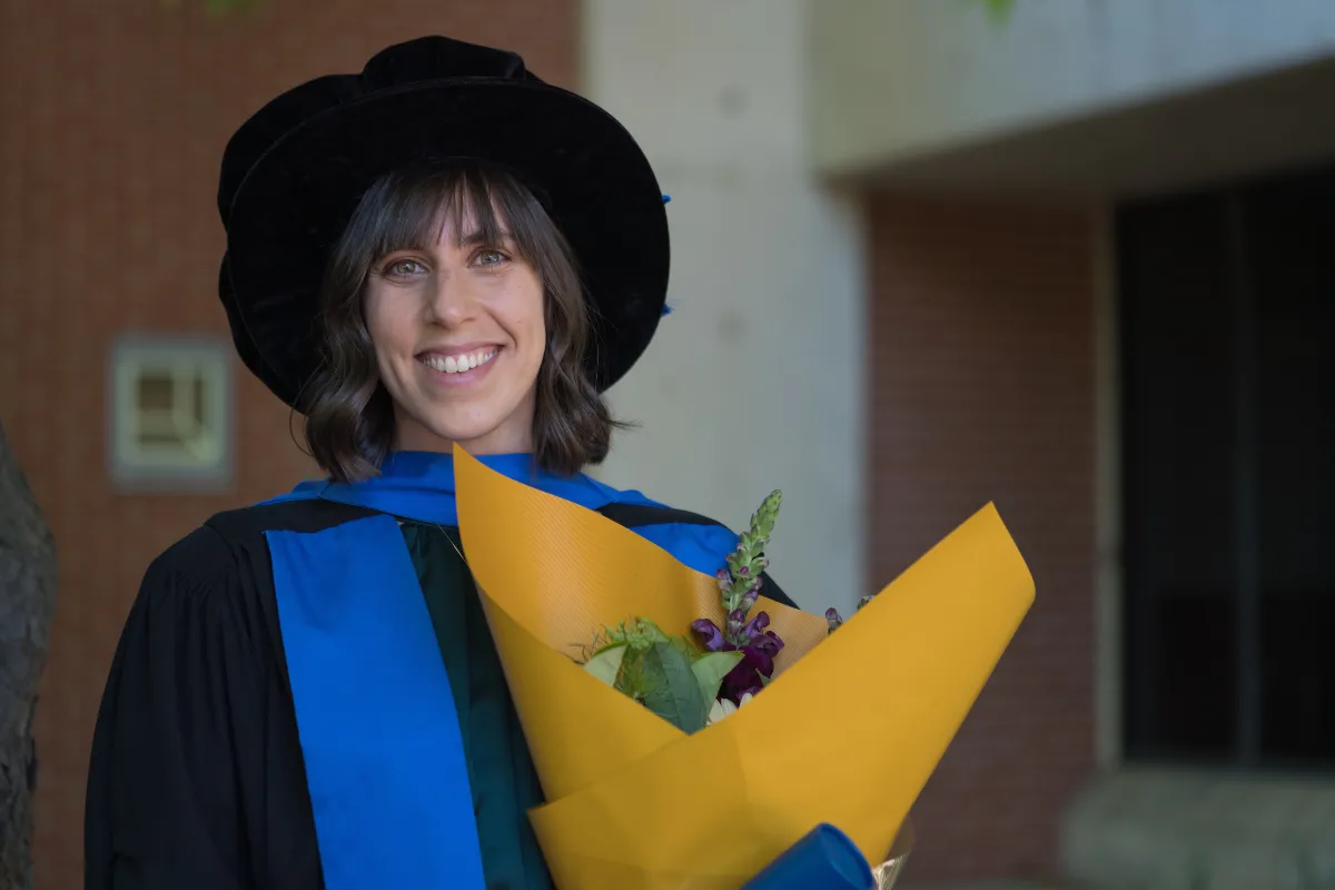 A woman in academic dress holding flowers