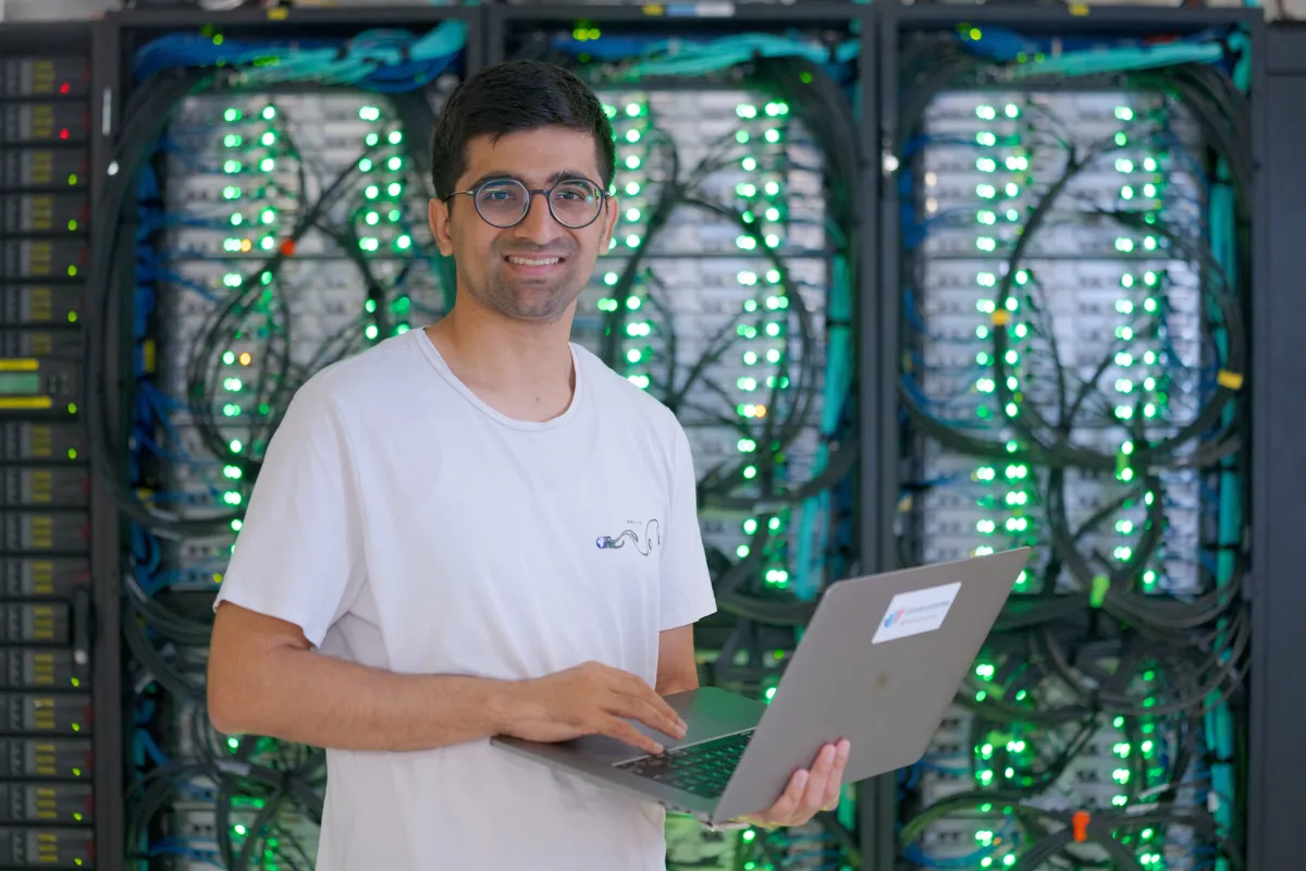 A man standing in front of computer servers with a laptop