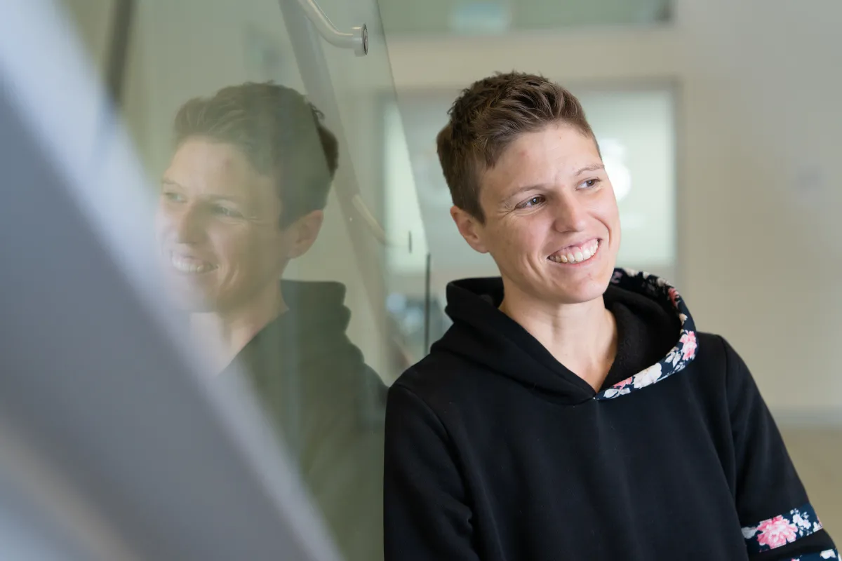 A smiling woman leaning against a glass staircase