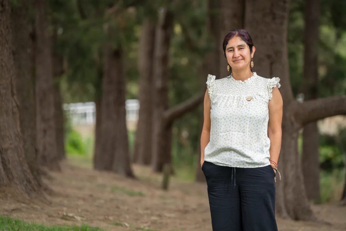 A woman in a white top standing in front of trees