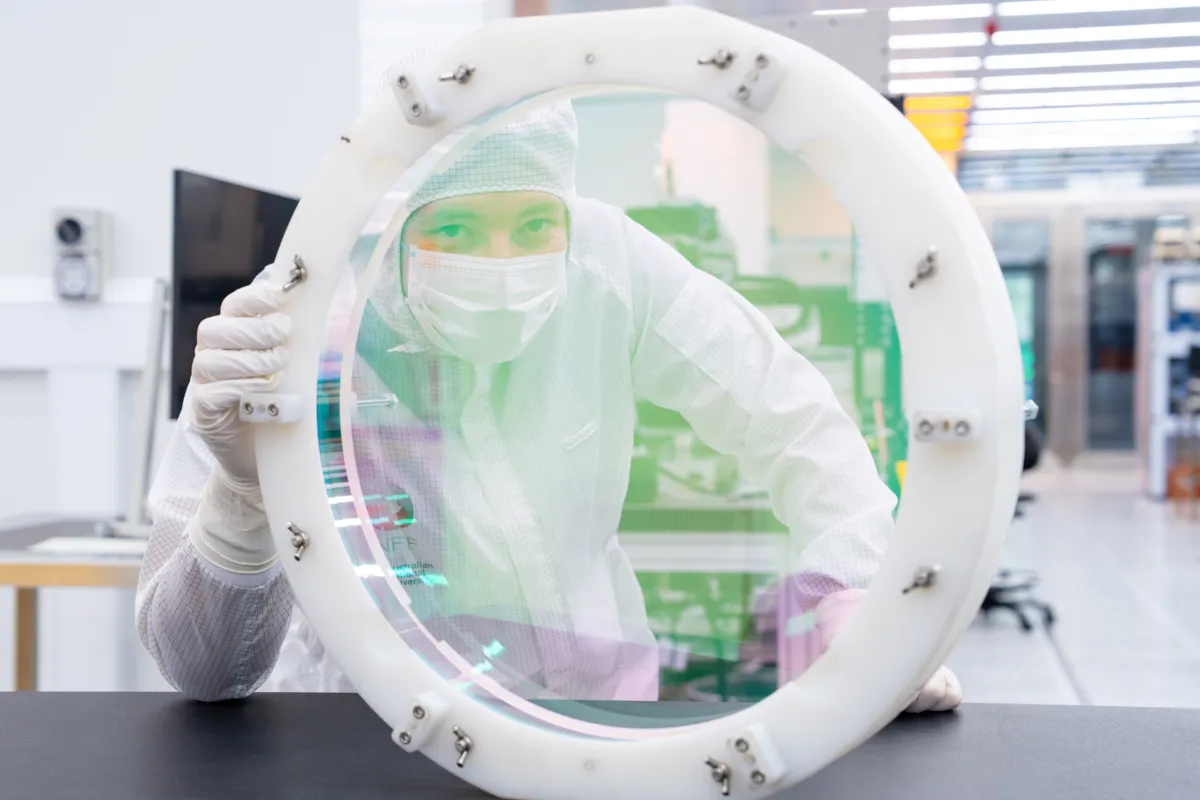 A scientist in a clean suit with a large piece of circular glass.