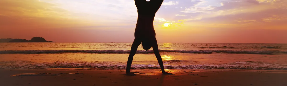 Silhouette of a person doing a handstand on the beach and sunset