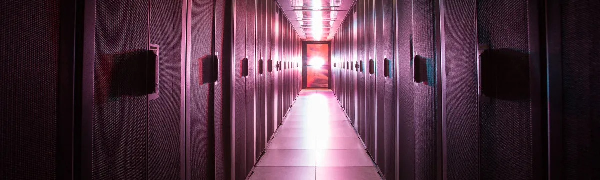 A brightly lit corridor with pink and purple lights, lined with electronic equipment on both sides.