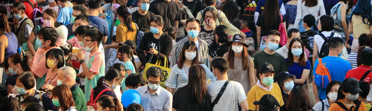 A large crowd of people wearing face masks gathered outdoors during daytime.