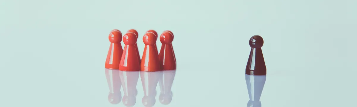 Five red game pawns grouped together opposite a single black game pawn on a reflective surface.