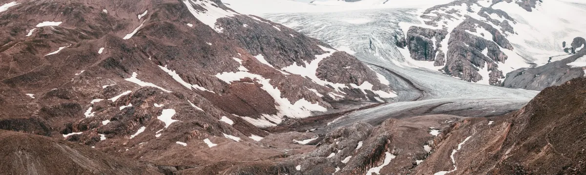 A glacial mountain landscape with a vivid turquoise lake in the foreground surrounded by rugged brown and snowy peaks.