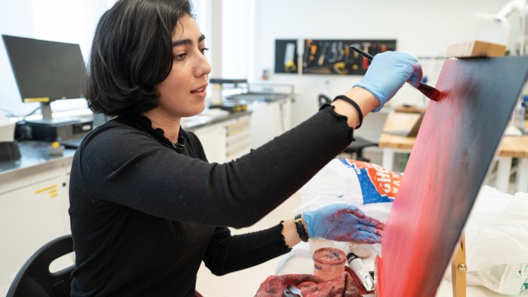 Raghda is painting a red artwork at an easel