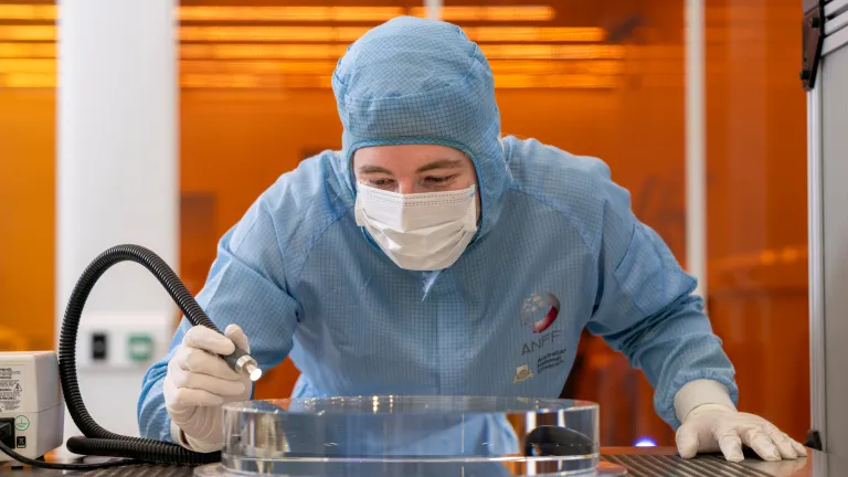 A scientist in a clean suit working at a metal bench.