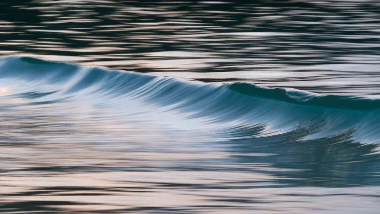 Photo of peaceful ocean waves captured at twilight with soft reflections.