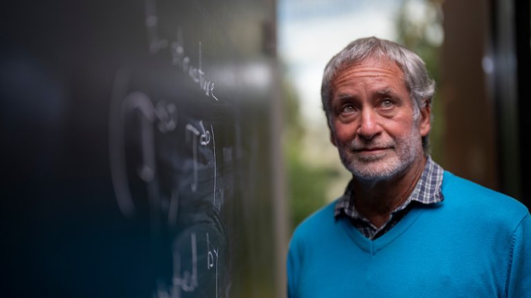 A man standing next to a blackboard, with maths equations on it