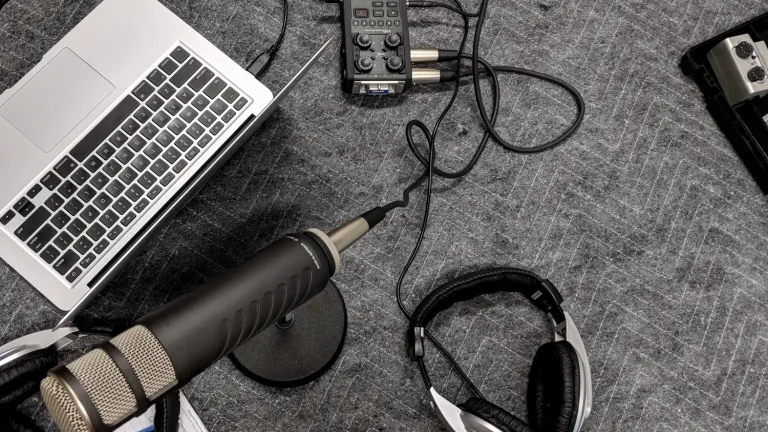 A laptop, microphone, audio interface, and headphones laid out on a gray carpet, suggesting a podcast recording setup.