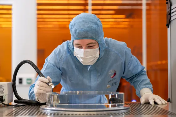 A scientist in a clean suit working at a metal bench.