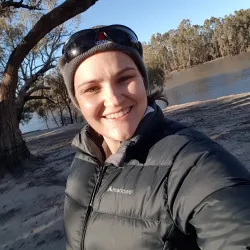 A smiling woman in a puffy jacket with a river in the background