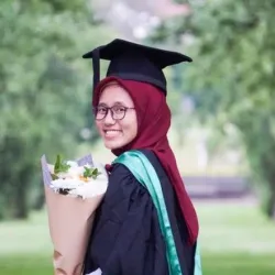 A woman in graduation cap and gown holding flowers and smiling