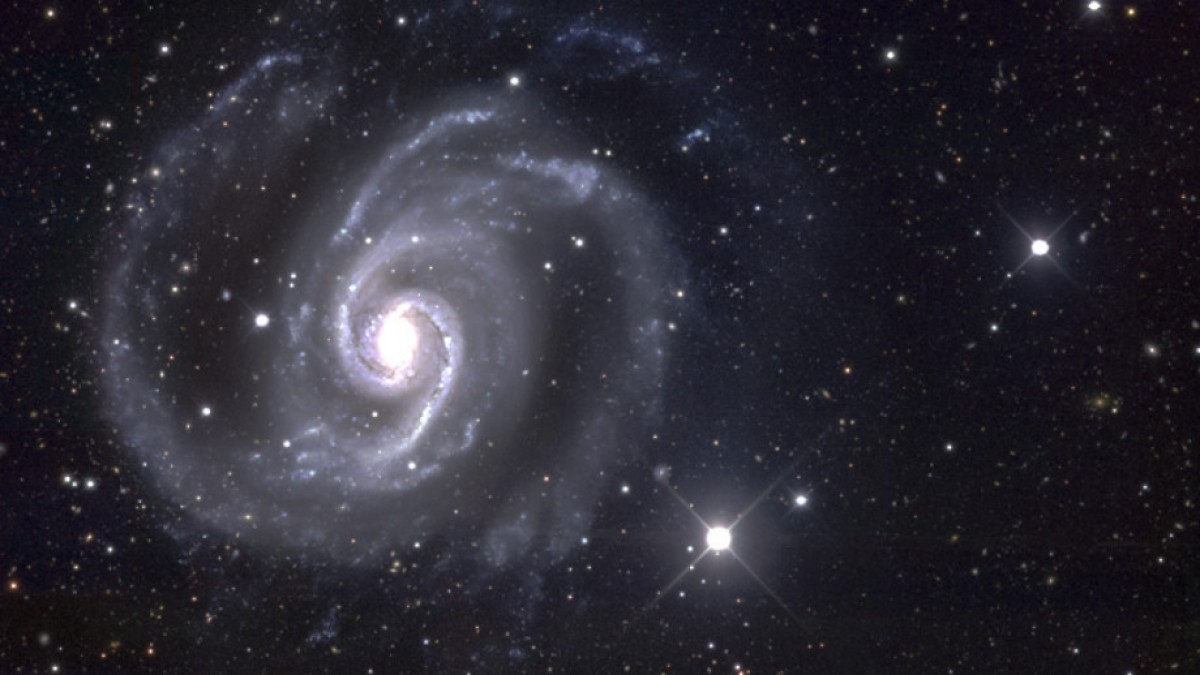 Telescope image of a spiral galaxy surrounded by white stars.