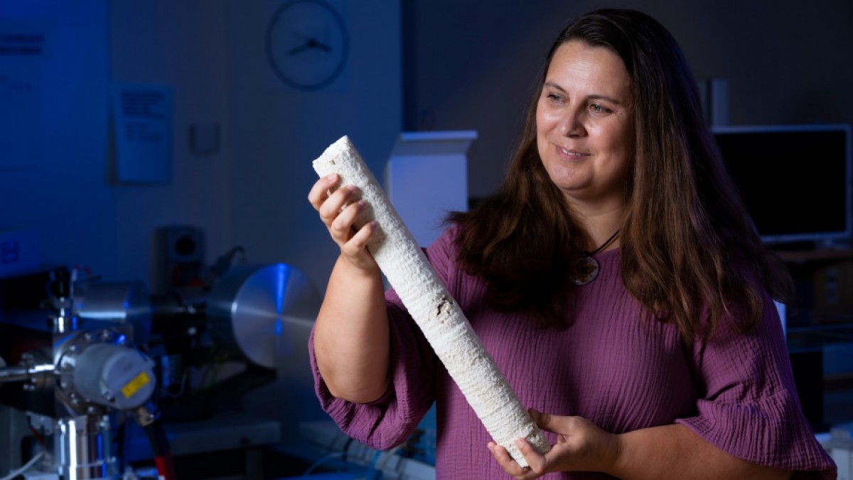 Professor Nerilie Abram is holding a coral core sample in laboratory lit with blue light