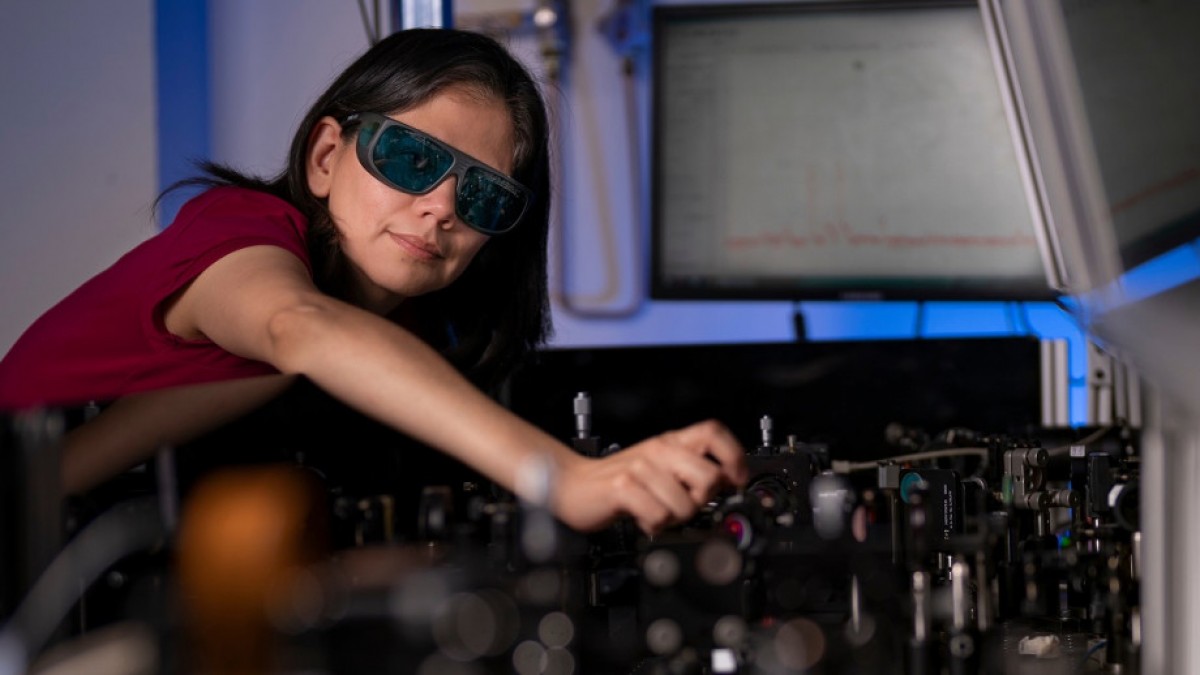 Dr Rocio Camacho Morales in physics lab, photographed leaning over a table with laser optics equipment.