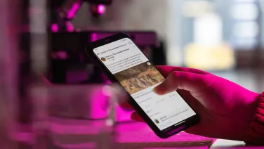 A hand in a lab holding a mobile phone showing a Facebook post about kangaroos