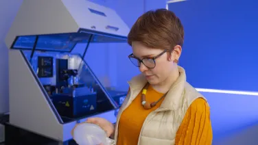A woman in glasses holding a mother of pearl shell with a microscope in the background