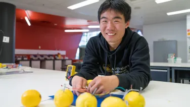A man in an ANU hoodie with a bunch of lemons and electrical equipment