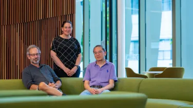 Two men seated on a green sofa and one woman standing