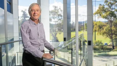 Professor Trevor Lamb inside a light filled foyer overlooking a green campus