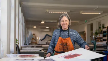 Susanne Ilschner in a printmaking studio holding artworks on paper