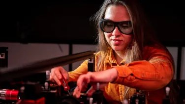 A woman with safety glasses working in a physics lab