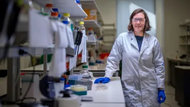 A woman in a lab wearing a lab coat and safety glasses