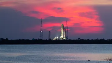 A rocket on a launchpad near water against a sunset