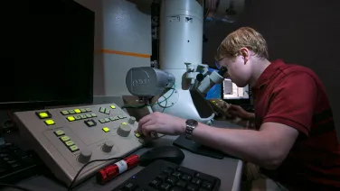 A person using an advanced microscope and control panel in a dimly lit laboratory.