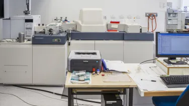 An image of a modern laboratory with various analytical instruments, a printer, a computer, and documents scattered over the worktables.